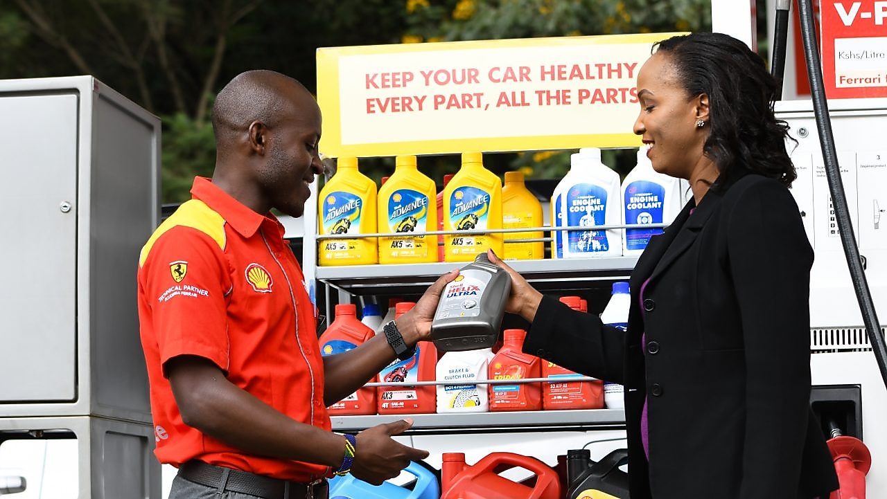 A red Ferrari sitting on a Shell station forecourt with a man leaning on a petrol pump